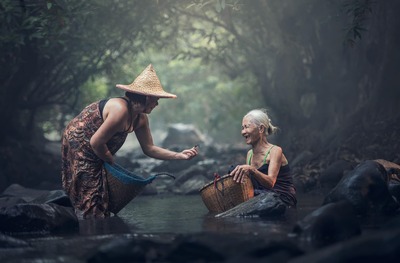 Duas mulheres com seus cestos de vime conversam no raso do riacho Duas mulheres com seus cestos de vime conversam no raso do riacho