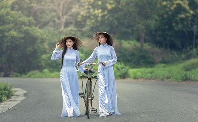 Duas jovens mulheres caminhando sorridentes levam a bicicleta entre elas Duas jovens mulheres caminhando sorridentes levam a bicicleta entre elas
